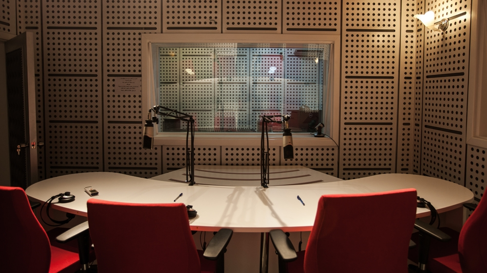 Interior of a modern recording studio featuring a circular table with red chairs, microphones, and soundproof walls.